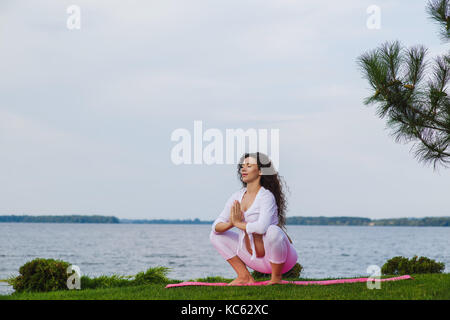 Schwangeren Yoga. Frauen, die verschiedenen Übungen im Park auf der Wiese, Atmung, Dehnung, Statik. Wald und Fluss auf Hintergrund. Konzept der Gesundheit Stockfoto