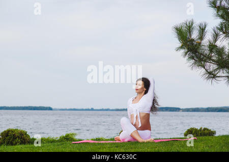 Schwangeren Yoga. Frauen, die verschiedenen Übungen im Park auf der Wiese, Atmung, Dehnung, Statik. Wald und Fluss auf Hintergrund. Konzept der Gesundheit Stockfoto