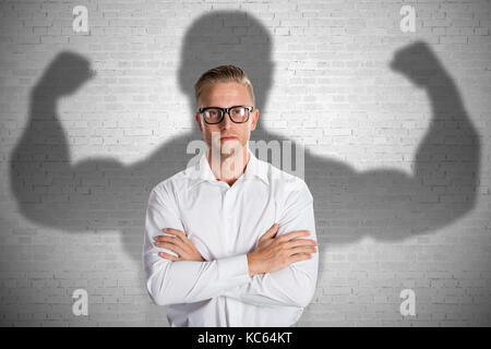 Konzeptionelle junge Unternehmer stehen vor grauem Hintergrund mit muskulösen Schatten Stockfoto