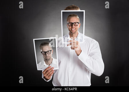 Traurige Mann, Lächeln Bild Vor seinem Gesicht auf schwarzem Hintergrund Stockfoto