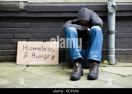 Obdachlose und Hungrige Menschen sitzen auf der Straße mit Namensschild Stockfoto