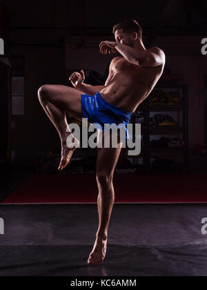 Ein männlicher MMA Fighter Training Kicks und Schläge in einer dunklen Fitnessraum Stockfoto