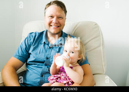 Vater feeding baby girl (12-17 Monate) im Wohnzimmer. Stockfoto