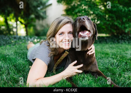 Porträt der lächelnde Frau liegend auf Gras mit Labrador Retriever Stockfoto