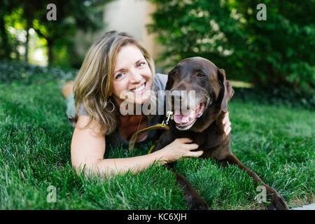 Porträt der lächelnde Frau liegend auf Gras mit Labrador Retriever Stockfoto