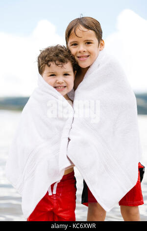 Portrait von Brüdern (4-5, 6-7) in Handtücher stehen am See gewickelt Stockfoto