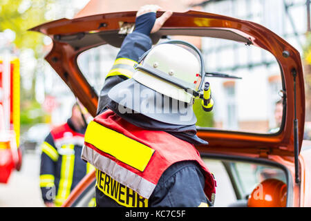 Deutsche Feuerwehrmann mit Helm hält seine Hand auf dem Kofferraumdeckel Stockfoto