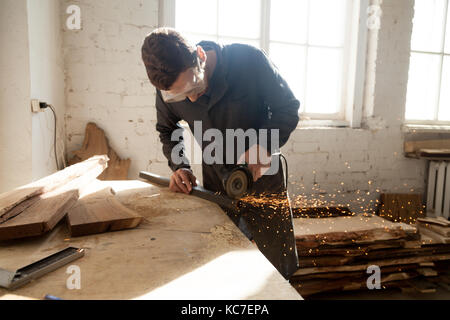 Handwerker in Schutzbrille Schneiden von Stahl plank auf der Workbench mit Winkelschleifer in Werkstatt. Schreiner mit der Arbeit an einem neuen Projekt starten Eigene Stockfoto