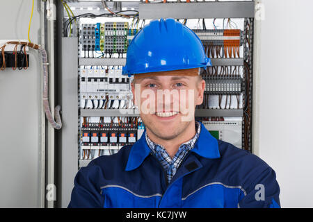 Portrait eines glücklichen jungen männlichen Elektriker Stand vor der Sicherungskasten Stockfoto