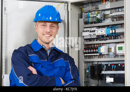 Portrait eines glücklichen jungen männlichen Elektriker Stand vor der Sicherungskasten Stockfoto