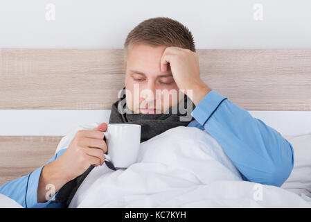 Junger Mann im Bett mit Decke und eine Tasse heiße Getränke Stockfoto