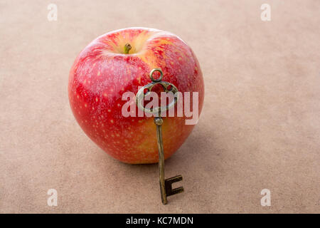Hand mit einem Schlüssel neben einem roten Apfel Stockfoto