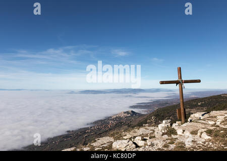 Ein hölzernes Kreuz auf der Spitze des Monte Subasio Berg, mit einem Meer von Nebel unten Stadt Assisi (Umbrien) im Hintergrund und Stockfoto