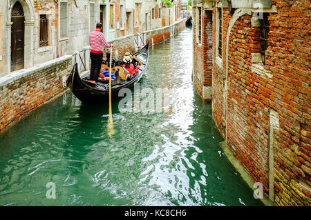 Ein gondoliere nimmt eine Gruppe von Touristen auf einem schmalen Kanal in Venedig, Italien Stockfoto