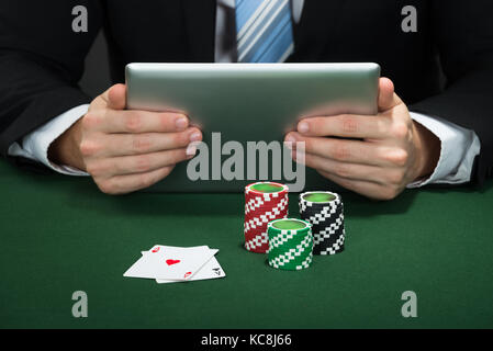 Poker Hand mit digitalen Tablet mit Chips und Karten auf dem Tisch Stockfoto