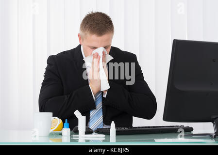 Sick Geschäftsmann bläst seine Nase im Büro mit Medikamenten auf Schreibtisch Stockfoto