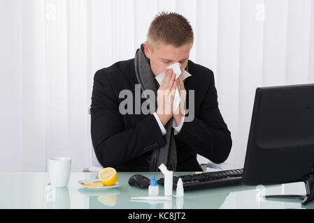 Sick Geschäftsmann bläst seine Nase im Büro mit Medikamenten auf Schreibtisch Stockfoto