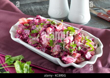 Salat mit gekochte rote Bete, Kartoffeln, Gurken, Zwiebeln in eine weiße Platte auf einer Textur Hintergrund Stockfoto