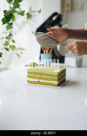 Grüner Tee Pulver über leckeren Käsekuchen gießen Stockfoto