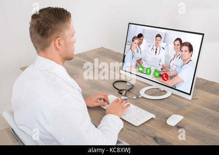 Junge männliche Arzt Videokonferenzen mit medizinischen Team auf dem Schreibtisch, in der Klinik Stockfoto