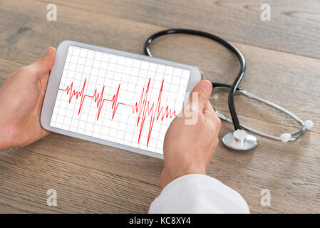 Nahaufnahme der männlichen Arzt mit heartbeat auf digital Tablet mit Stethoskop auf hölzernen Schreibtisch Stockfoto