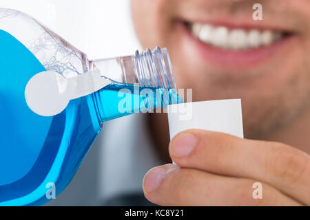 Close-up des jungen Mannes Gießen Flasche Mundspülung in den Deckel Stockfoto