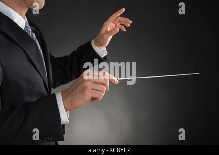 Person Regie mit einem Taktstock auf grauem Hintergrund Stockfoto