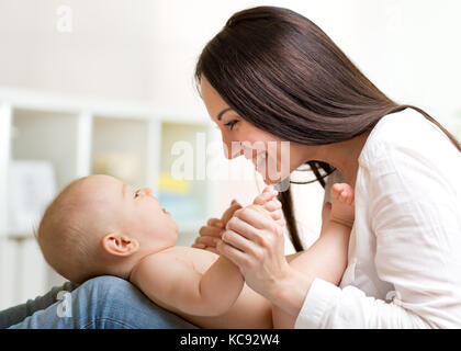 Charmante Baby bei Mama schauen und lächeln beim Lügen auf die Knie seiner Mutter. glückliche Mutter an ihr Kind, der Sohn ist auf der Suche Stockfoto