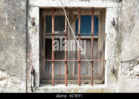 Ein altes Verfallenes bauernhaus rustikal gebrochenen Fenster im faulen alten Hölzer und Bars an der Vorderseite eingestellt. einem vergitterten Fenster im Shabby Chic Stil für die Sicherheit. Stockfoto