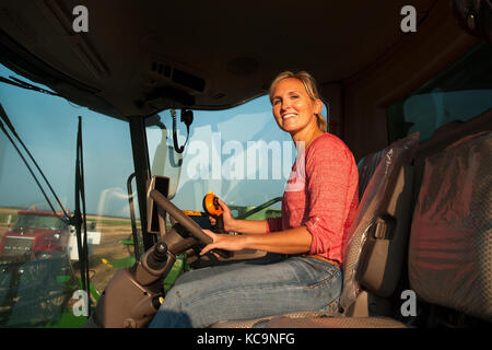 Eine junge weibliche Landwirt sitzt IN EINEM JOHN DEERE MÄHDRESCHER VOR DER ERNTE VON WEIZEN AUF DEM BAUERNHOF DER FAMILIE IN DER NÄHE VON BRECKENRIDGE, NORTH DAKOTA Stockfoto