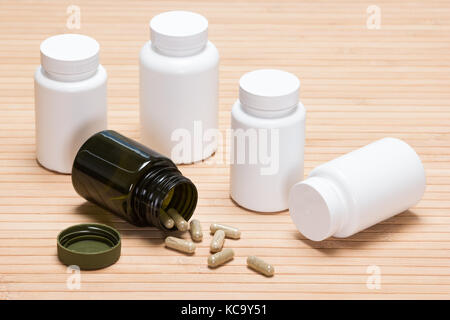 Öffnen Sie Dunkelgrün jar mit verstreuten Kapseln von weißem Kunststoff Gläser von Arzneimitteln umgeben umgeworfen Stockfoto