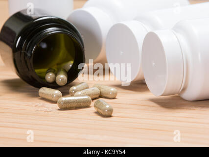Close-up umgeworfen öffnen Dunkelgrün jar mit verstreuten Kapseln von weißem Kunststoff Gläser von Arzneimitteln umgeben. Seitenansicht Stockfoto
