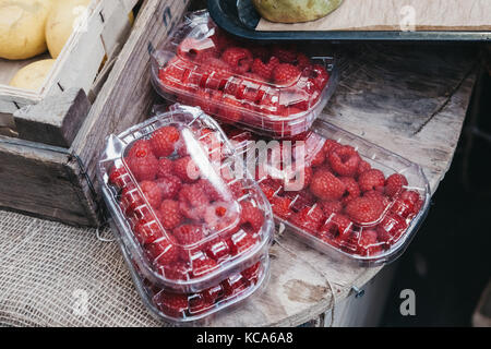 Frische Himbeeren auf Verkauf in Kunststoffkästen, auf einem Holztisch Stockfoto