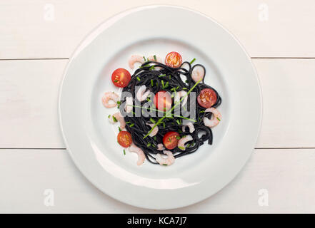 Squid Tinte schwarz Pasta mit Garnelen, Schnittlauch und Tomaten auf weißem Hintergrund Stockfoto