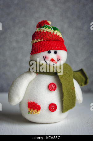Lächelnd schneemann Spielzeug in Schal und Mütze auf abstrakte bokeh Hintergrund gekleidet. Stockfoto