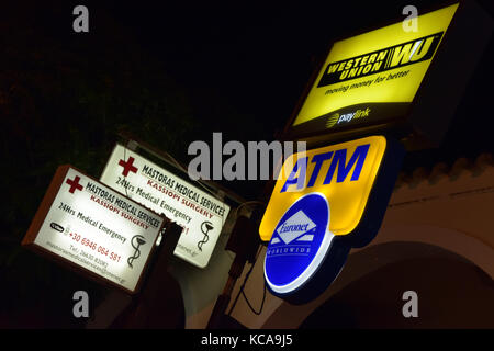 Beleuchtete Schilder in einem Einkaufsviertel von Kassiopi auf der griechischen Insel Korfu. Urlaub Versicherung und medizinische Dienste Western Union Money Services ATM Stockfoto