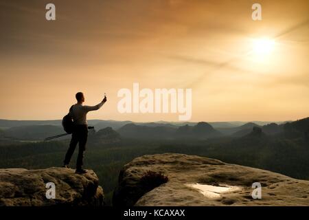 Scharfe Silhouette der aktiven Mann oben auf dem Berg mit Sonne im Rahmen. Wanderer mit Sportlicher Rucksack stand auf Rocky View Point oben misty Vall Stockfoto