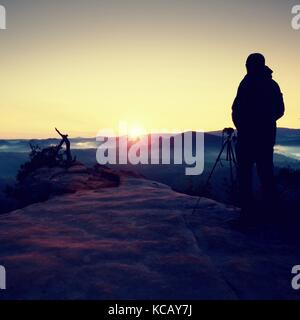 Silhouette der Landschaft Fotograf auf Spitze oben misty Valley. bunte Sonne heben über neblige Landschaft. Stockfoto