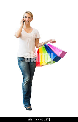 Junge lächelnde Frau mit Handy beim Tragen Shopping Bag auf weißem Hintergrund Stockfoto