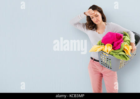 Junge müde Frau Tragekorb mit Kleidung auf farbigem Hintergrund Stockfoto