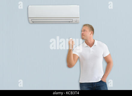 Junger Mann mit Fernbedienung Vor der Klimaanlage zu Hause Stockfoto