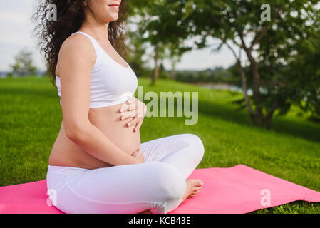 Schöne junge Schwangere Yoga im Park. schwangere Frau mit Händen über den Bauch. Stockfoto