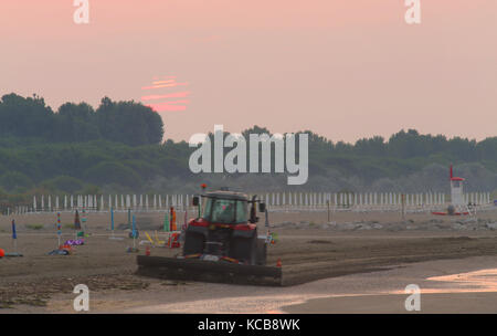Big Traktor, der sich in der Morgendämmerung den Strand reinigt aus dem Müll vom Vortag Stockfoto