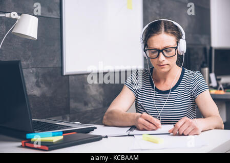 Frau tragen Brillen schreiben und Musik hören im Büro Stockfoto