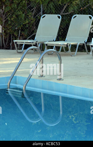 Zwei Sonnenliegen am Pool und die Reflexionen in das klare blaue Wasser mit etwas Handläufe und Schritte für die Eingabe des Wasser. Stockfoto