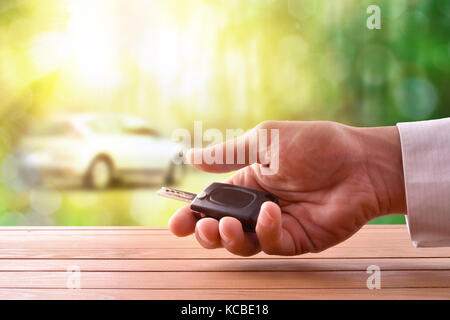 Hände mit Autoschlüssel auf einem Holztisch mit Auto Bild auf Natur Hintergrund. Konzept der Auto kaufen Stockfoto