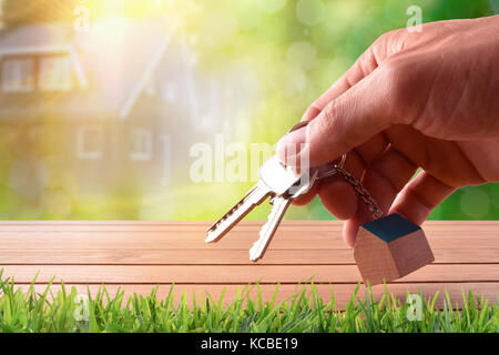 Schlüssel in der Hand auf einem Holztisch mit Haus Bild auf Natur Hintergrund. Konzept der Haus Kauf Stockfoto