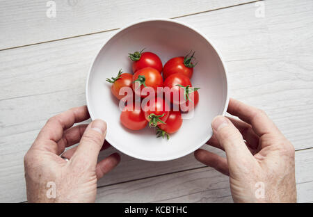 A bemannt Händen herauf eine weiße Schale, leuchtend rote reife Tomaten auf einer Arbeitsfläche aus hellem Holz, Arbeitsplatte in der Küche. Stockfoto