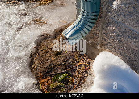 Aluminium Dachrinne auf der Mauer tropft Wasser in Schnee und Eis im Frühjahr. Stockfoto