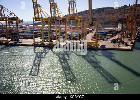Luftaufnahme der Schatten von großen, riesige Kräne auf der Meeresoberfläche in Barcelona Port. Viele Container sind im Hintergrund. Stockfoto